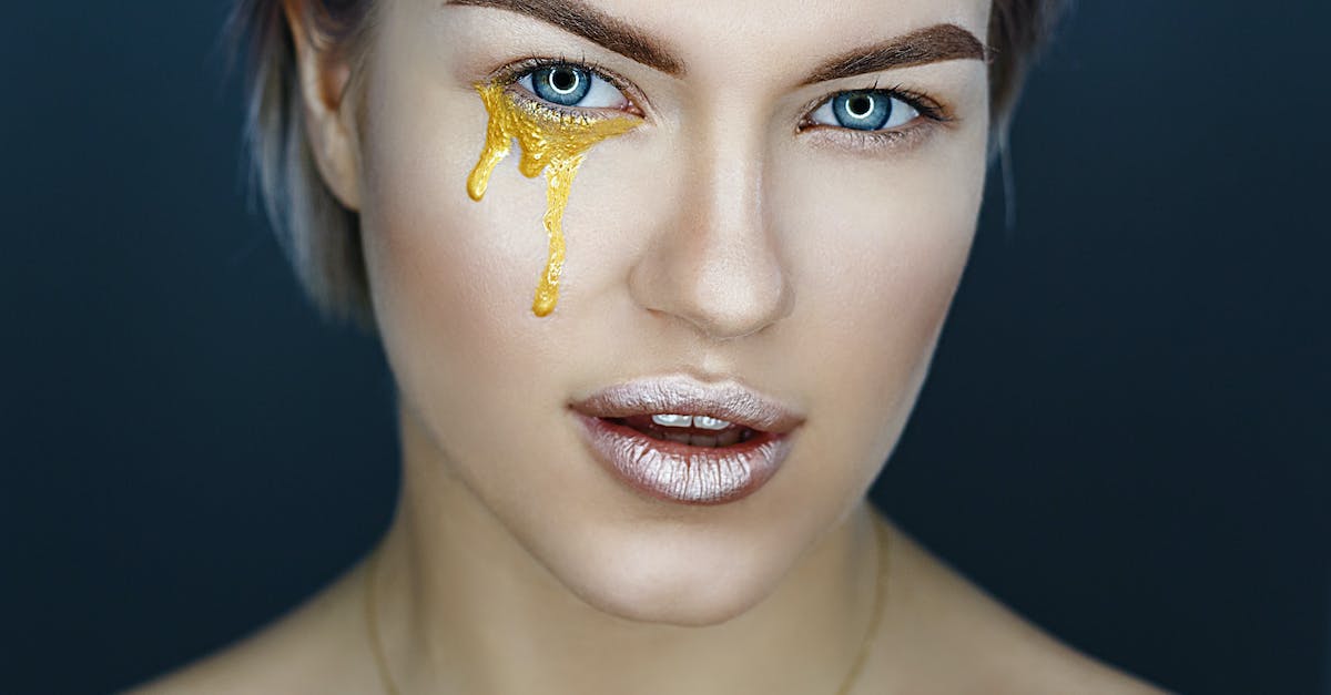 How to transfer gold between my characters? - Female model with gold paint of artistic makeup under eye and metal lipstick on lips looking at camera