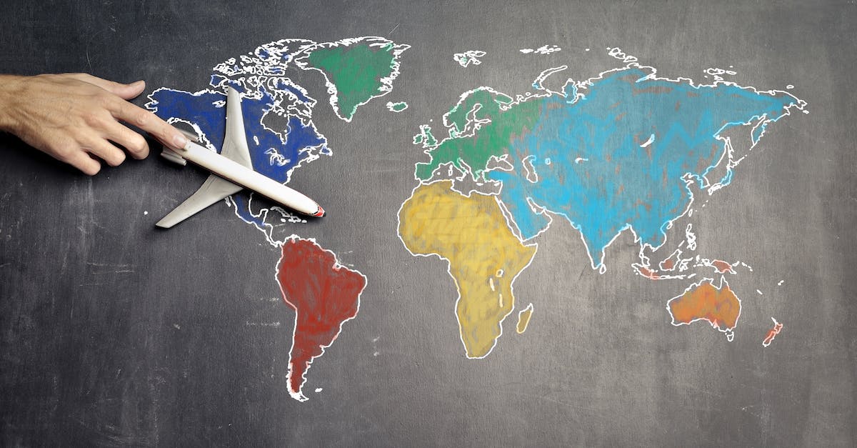 How to transfer my Minecraft Pocket Edition world from Android to iOS? - Top view of crop anonymous person holding toy airplane on colorful world map drawn on chalkboard