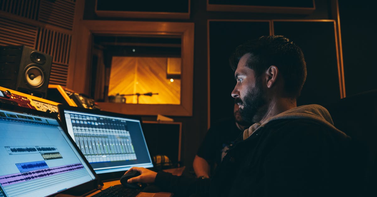 How to use hotkeys when focused program disables them? - Side view of concentrated ethnic bearded soundman working on computers with musical program on screens while creating arrangement sitting at table near colleague in music studio