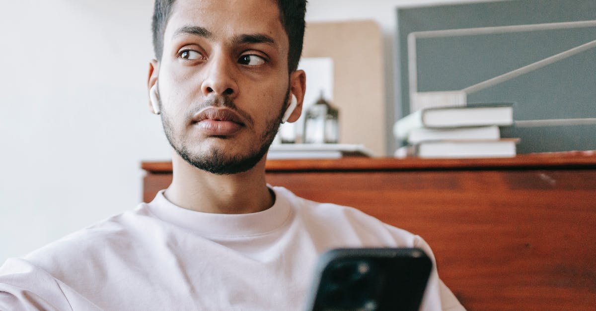 How to use PS4 controller's audio output via Bluetooth on PC? - Serious Indian man listening to music in wireless earbuds looking away while texting message on cellphone in light room against table with books