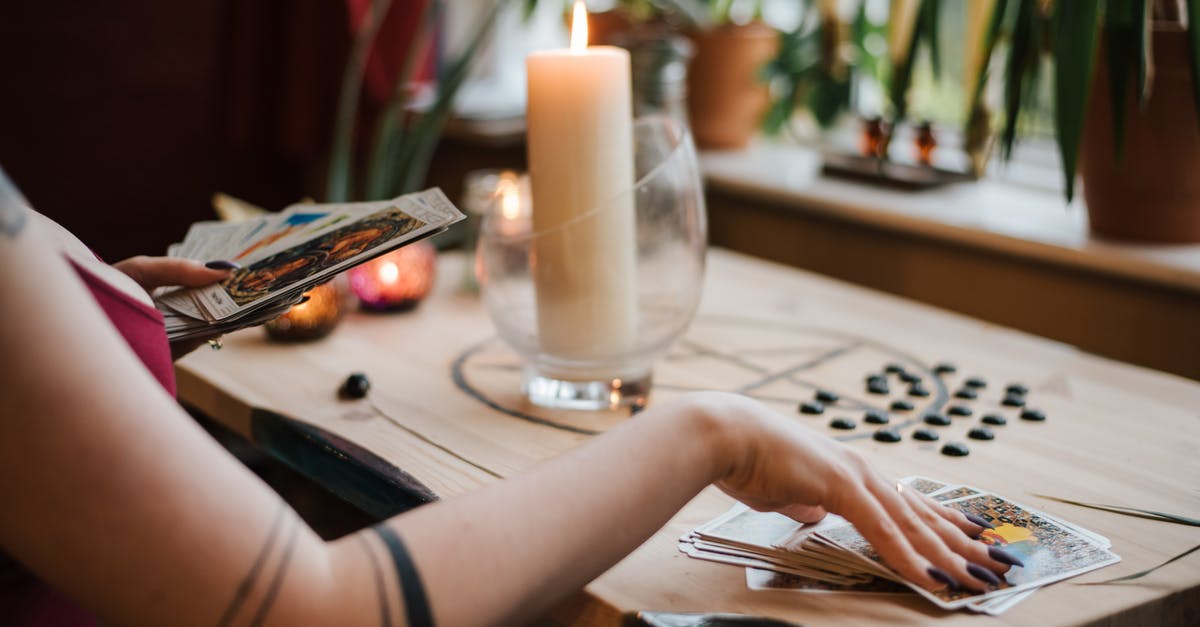 How was the house set on fire? - Crop unrecognizable fortune teller predicting fate with tarot cards near shiny candle at home