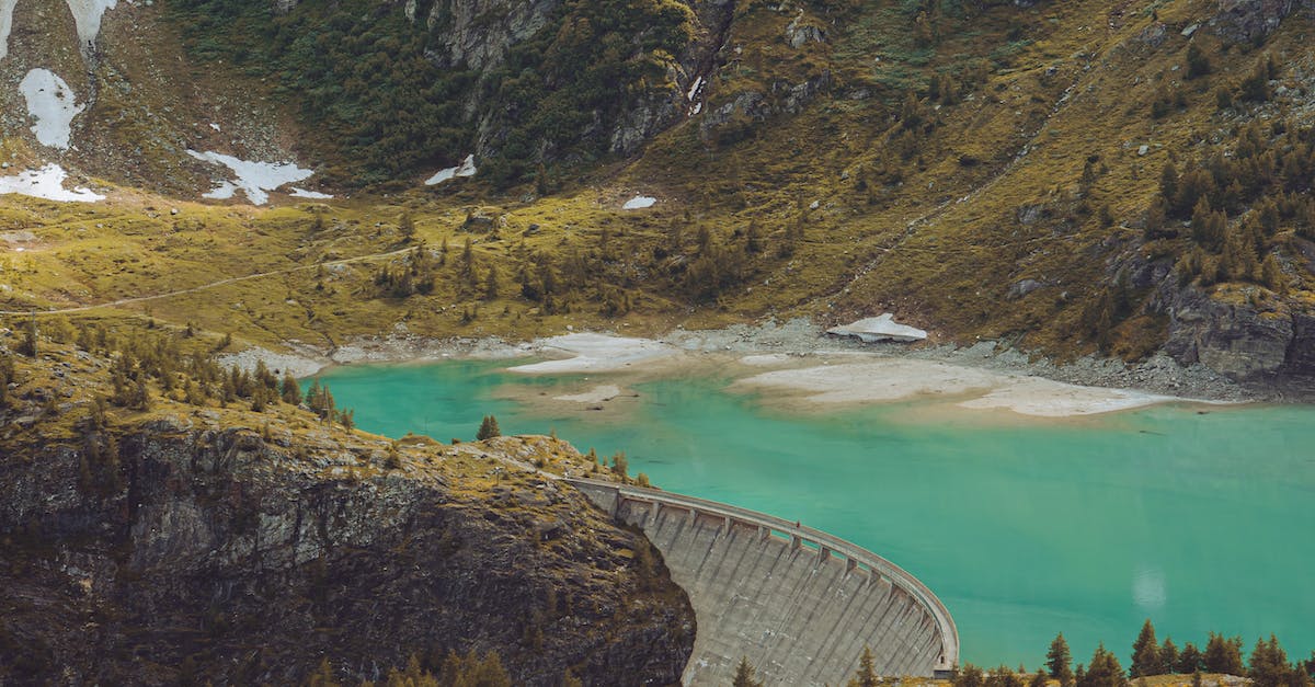 Hydro Plant not allowing water flow through - Spectacular scenery of dam near azure water in mountains covered with green grass and trees in daytime Hydro Plant not allowing water flow through - Spectacular scenery of dam near azure water in mountains covered with green grass and trees in daytime
