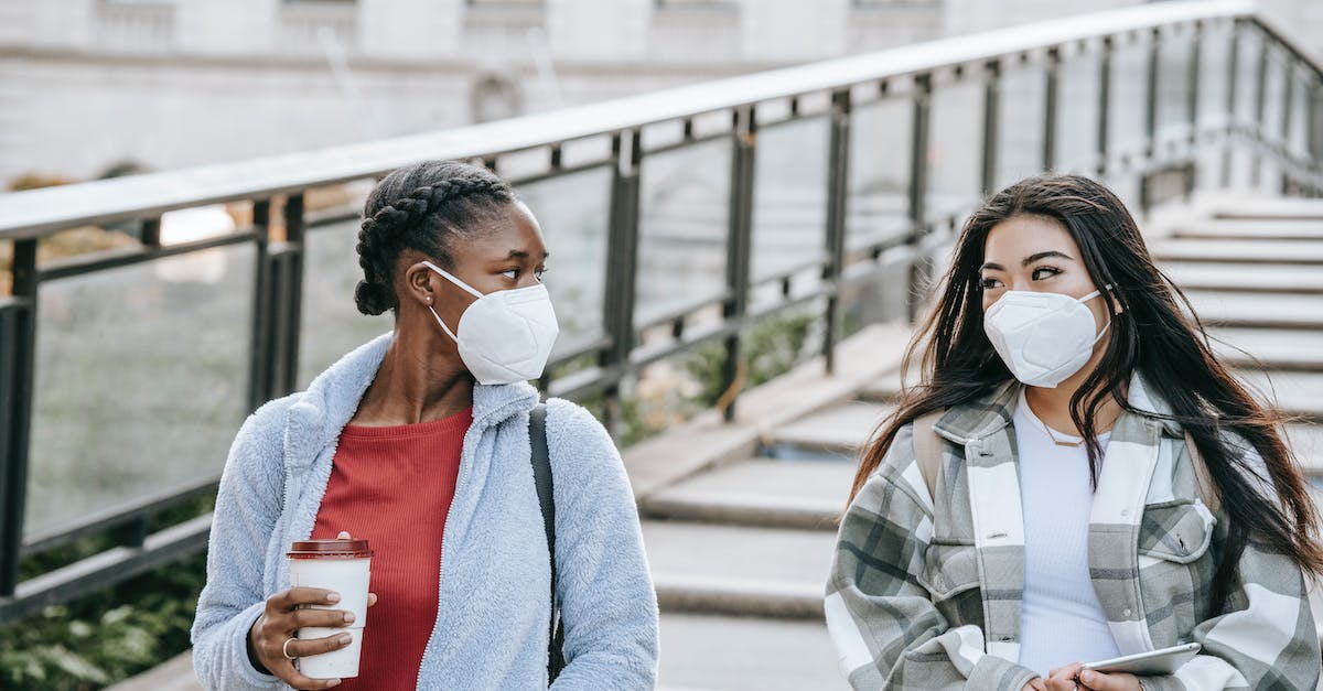 I'm able to go to other towns on ACNL, but one of my friends can't visit my town? - Young anonymous multiracial female friends in masks with tablet and hot drink to go looking at each other on city staircase