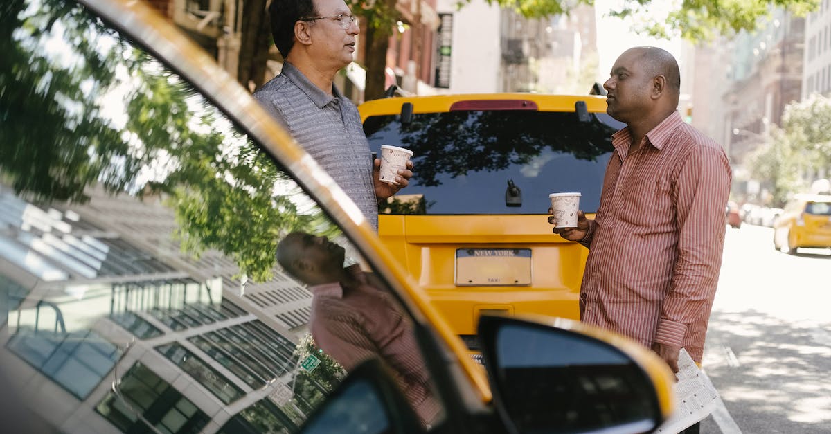 I'm able to go to other towns on ACNL, but one of my friends can't visit my town? - Side view of multiracial male coworkers with takeaway coffee conversing near yellow automobiles on urban road while looking at each other