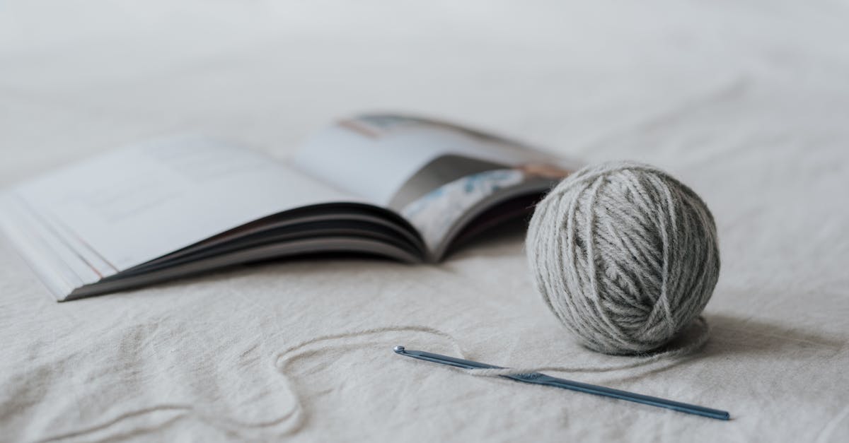 I've read an Auger recipe but I still can't craft one. Why? - Small spherical gray ball of threads and crochet needle with opened magazine on white fabric in bright room