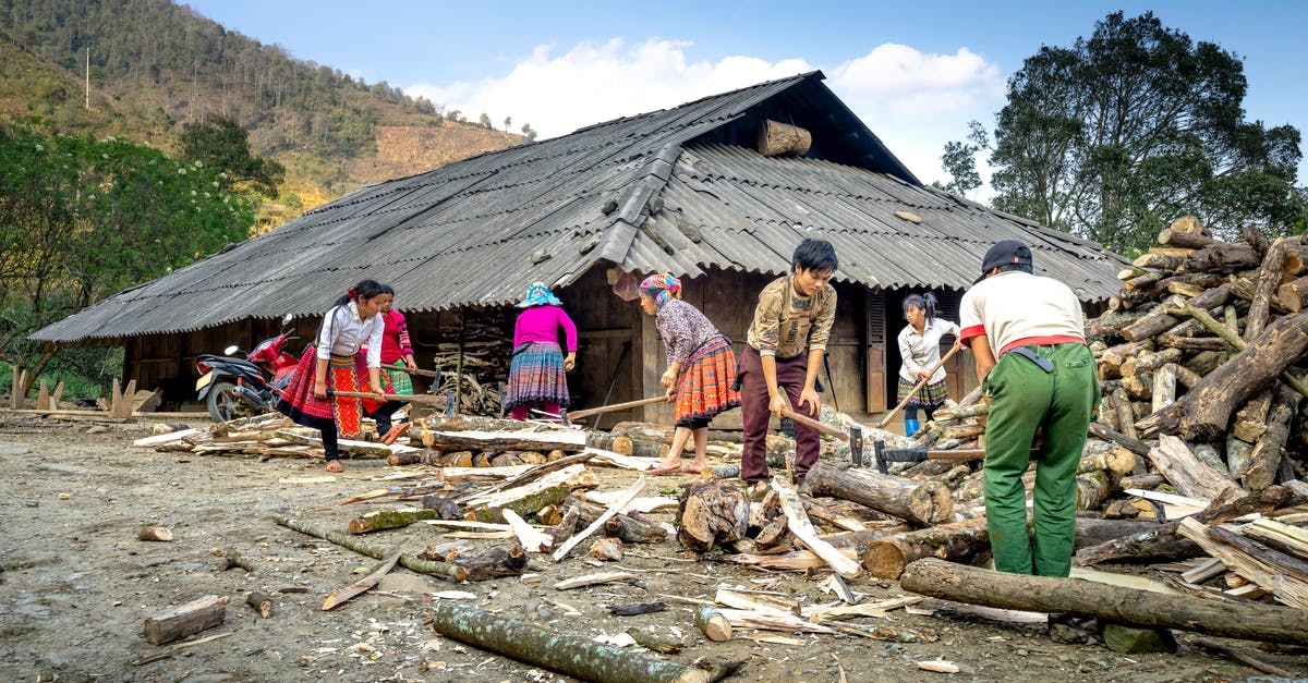 I can't find Chop at my house - Group of local Asian people working with firewood while standing in suburb area near shabby wooden hut against mountain ridge