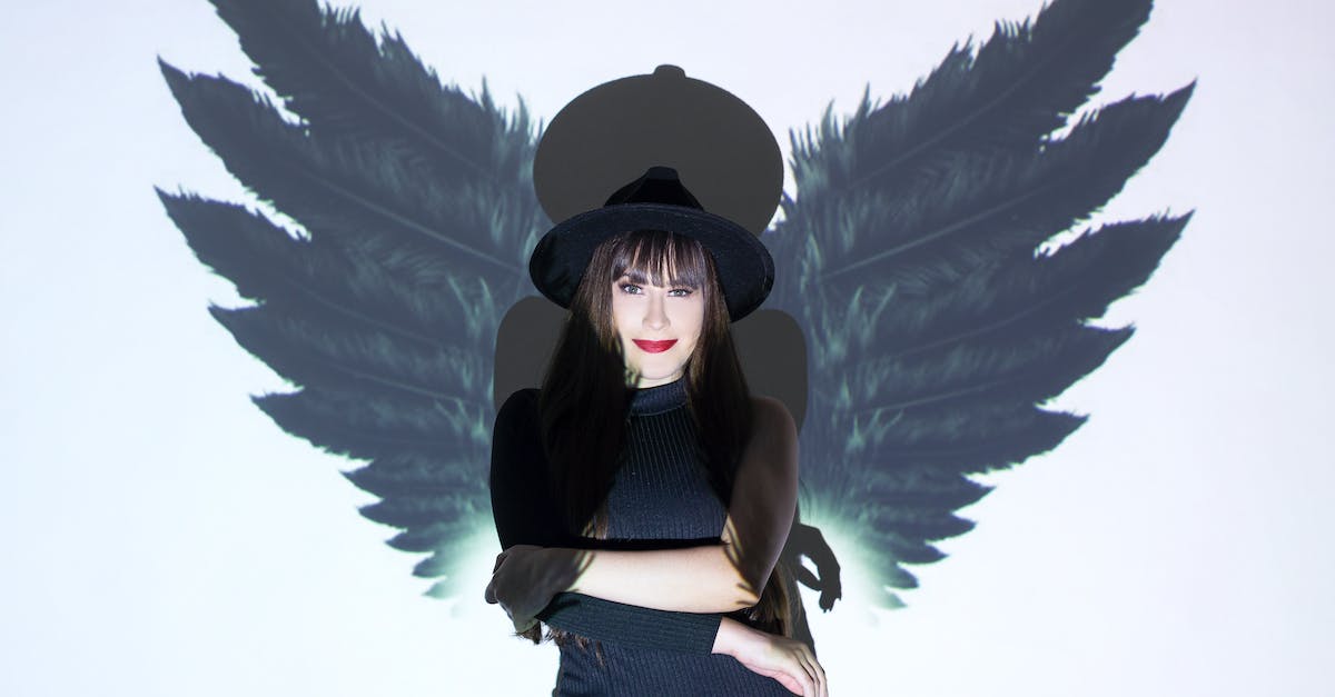 I can't see Shadow Demon and Warlock's Golem in DotA - Pretty female with dark hair in hat standing with crossed arms under light near wall with projecting wings and looking at camera while casting shadow on background