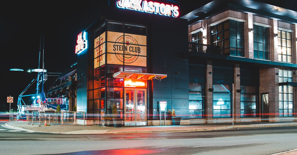 I killed a hostile mercenary in the Bar area and now everybody is hostile there! - Exterior of modern building with glass facade and illuminated signboard located near asphalt roadway at night