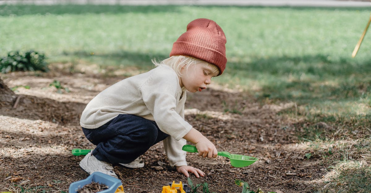 Identification of side-scrolling game - Side view of little boy in casual clothes and brown hat playing with plastic toys in backyard Identification of side-scrolling game - Side view of little boy in casual clothes and brown hat playing with plastic toys in backyard