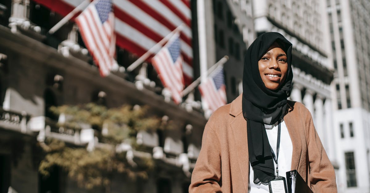 Identify building assets in-game - From below of cheerful African American female ambassador with folder wearing hijab and id card looking away while standing near building with American flags on blurred background