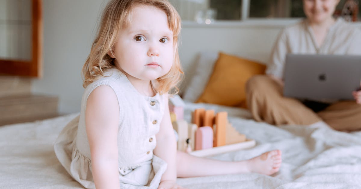 If I create a Game Center account, will I lose my village? - Cute toddler girl sitting and playing on bed while mother using laptop on background