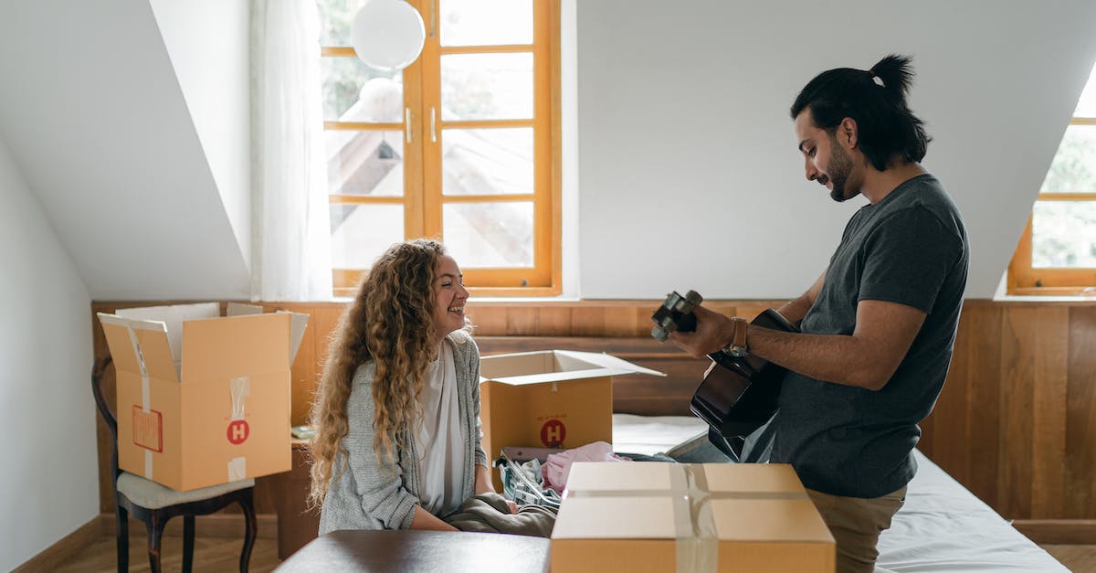If I purchase the Titanfall expansion pack(s), can I play with friends who have vanilla? - Side view of young bearded content husband playing guitar for smiling wife in bedroom while resting after packing stuff into carton boxes before relocation