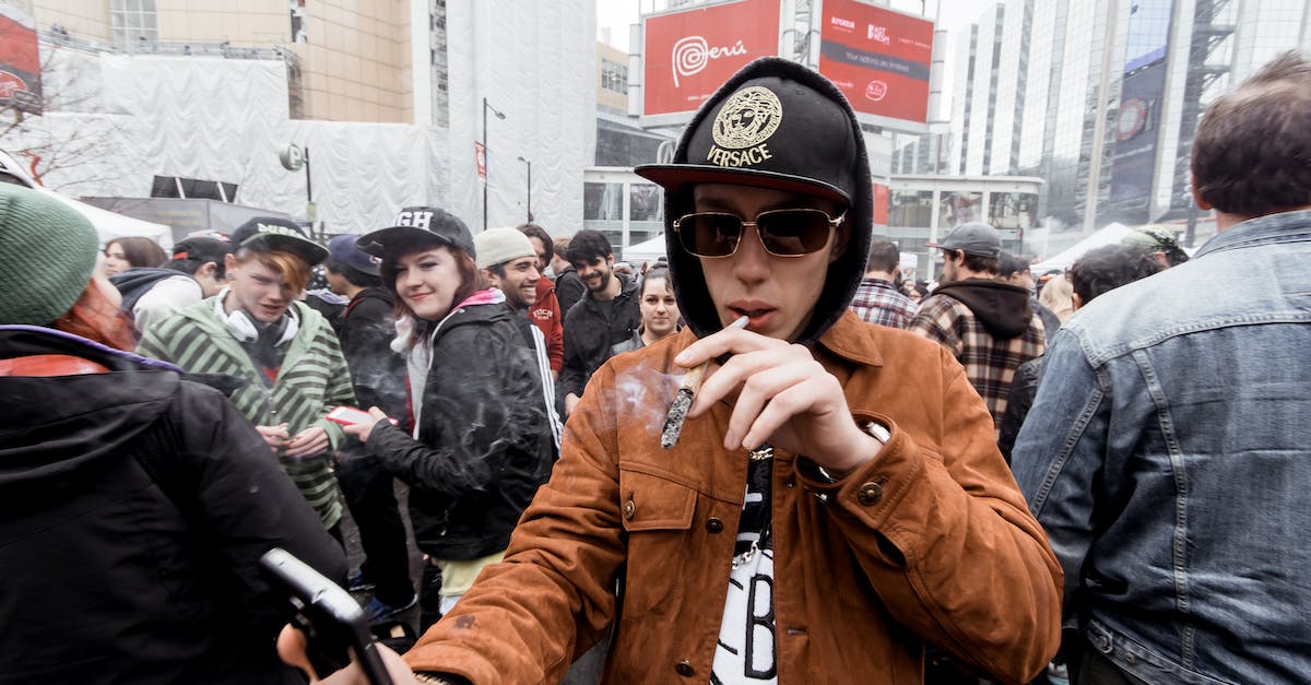 If I use cannons, will they be less effective against shields? - Young man in hat with hood standing on crowded street with smartphone in hand while smoking joint in city center If I use cannons, will they be less effective against shields? - Young man in hat with hood standing on crowded street with smartphone in hand while smoking joint in city center