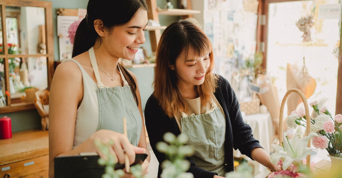 Implication of specialist step order - Optimistic multiethnic female colleagues in aprons standing near table with roses while making composition of flowers in floristry workshop during work
