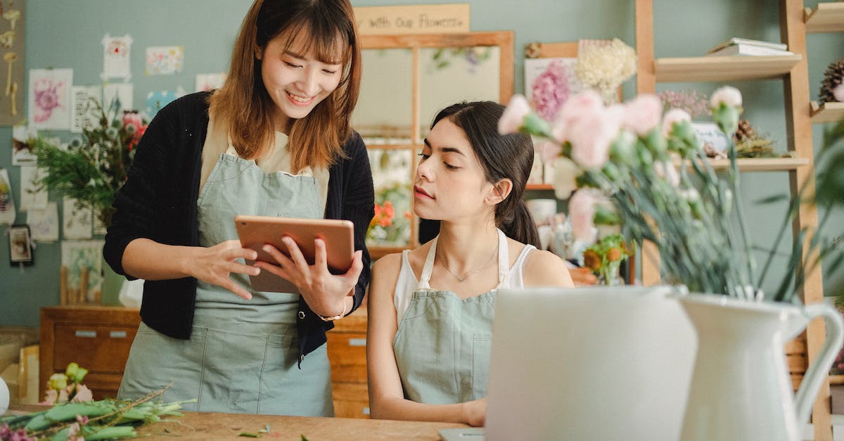 Implication of specialist step order - Content multiethnic female coworkers at table with flowers surfing tablet while choosing design for bouquet during work in florist shop