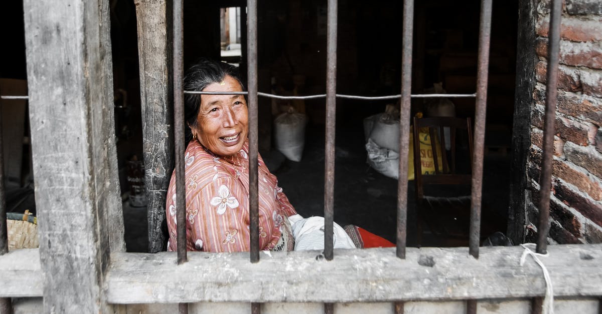 In WoW, how can I (via native features or add-ons) toggle between multiple spell bar configurations? - Side view of happy mature Nepalese female with dark hair smiling while sitting in old shabby house behind metal bars in countryside