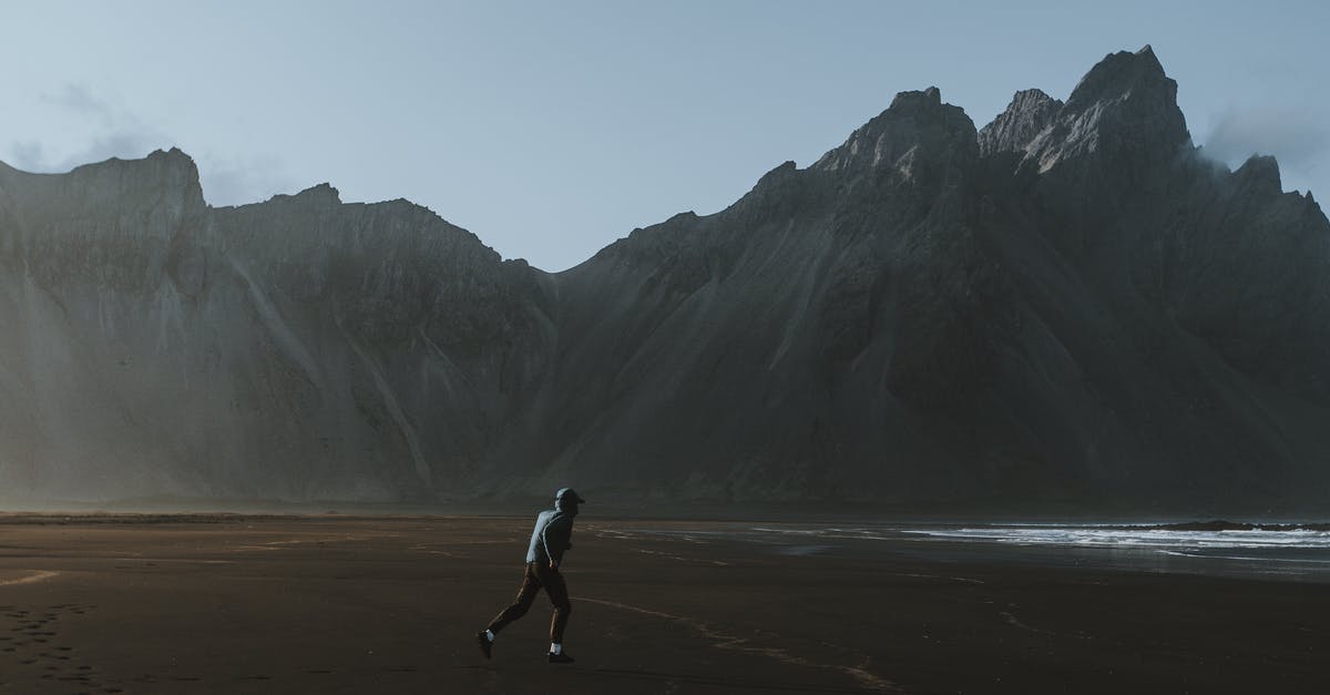 Increase cell loading range with distant landscape rendering off - Distant unrecognizable tourist in casual clothes walking on empty sandy beach towards mountain range Increase cell loading range with distant landscape rendering off - Distant unrecognizable tourist in casual clothes walking on empty sandy beach towards mountain range