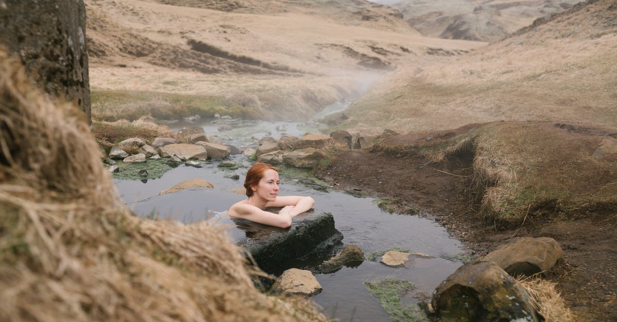 Infusing with faint stone vs. Infusing with Magic stone? - Side view of young red haired female leaning on big stone in pond with transparent water formed of narrow river flow passing between mounts covered with sand in mist