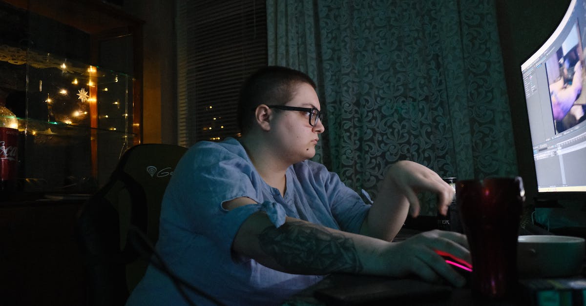 Internet functions appears disabled when game starts in the Atelier Plus games - Side view of obese young male in eyeglasses with tattooed arm sitting at table and using computer with curved monitor while spending evening at home