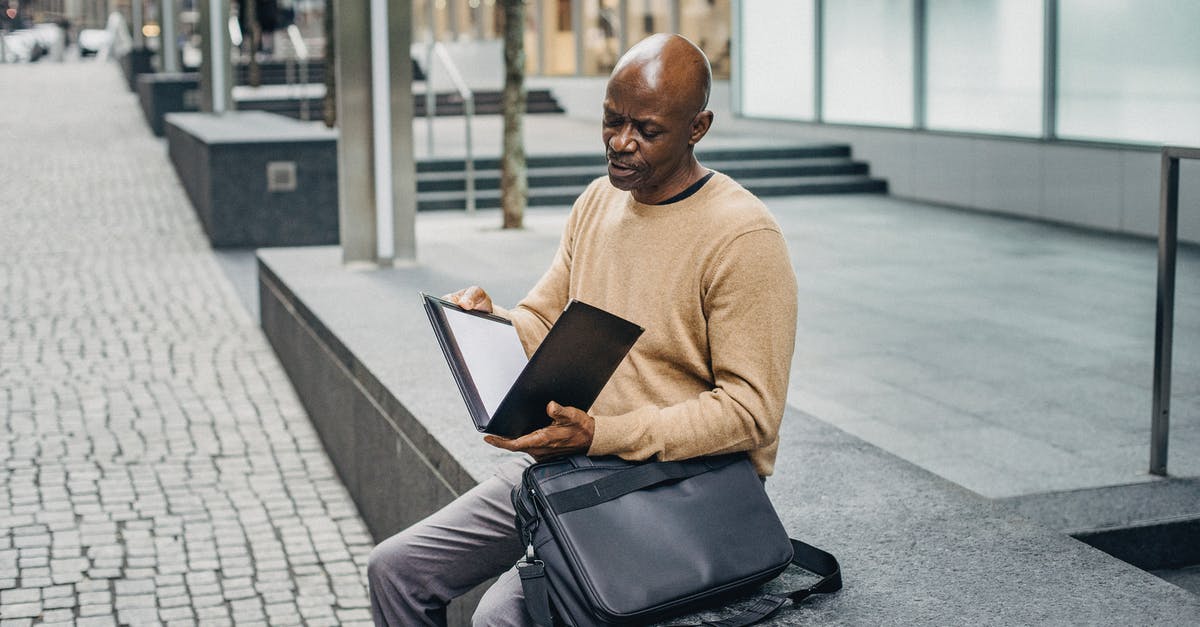 Is it a bug if my bag and my journal are contradicting? - Mature African American male opening folder with document while sitting on marble fence in downtown Is it a bug if my bag and my journal are contradicting? - Mature African American male opening folder with document while sitting on marble fence in downtown