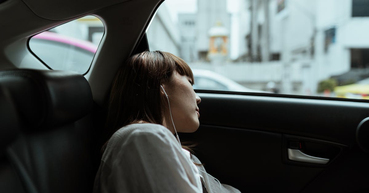 Is it dangerous to leave my car idling while I sleep in a garage? - Side view of unemotional female in white shirt resting in car passenger seat and listening to music via earphones while riding in urban environment Is it dangerous to leave my car idling while I sleep in a garage? - Side view of unemotional female in white shirt resting in car passenger seat and listening to music via earphones while riding in urban environment