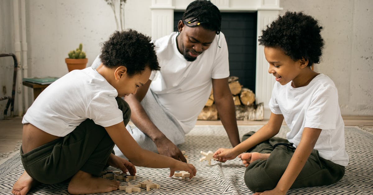 Is it easier to have aliens of similar races on your planet? - Happy young African American father in casual outfit smiling while sitting on floor and playing with wooden toys with positive twin sons during weekend at home