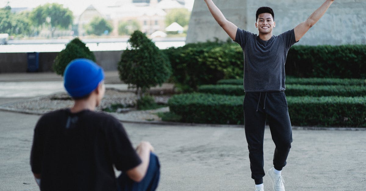 Is it possible to achieve open NAT (Type 1) on my PS4? - Happy smiling Asian man raising arms in satisfaction while spending sunny day outside with friend and looking at camera