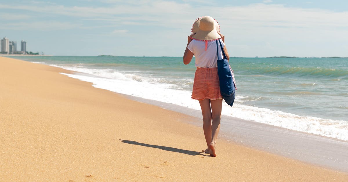 Is it possible to adjust your walk speed? - Full body back view of barefoot female traveler in casual clothing adjusting hat while waking on sandy coast of wavy ocean at resort