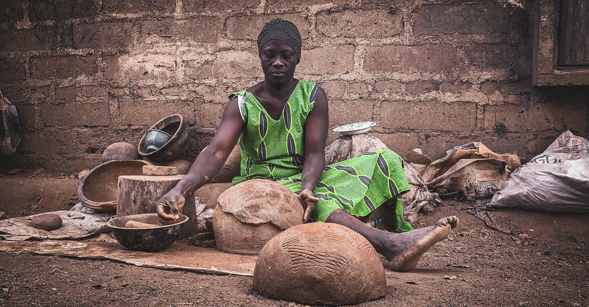 Is it possible to create a Villager who sells pufferfish? - Serious barefooted adult African woman in rustic authentic dress and turban sitting on ground near shabby wall and creating traditional handicraft earthenware