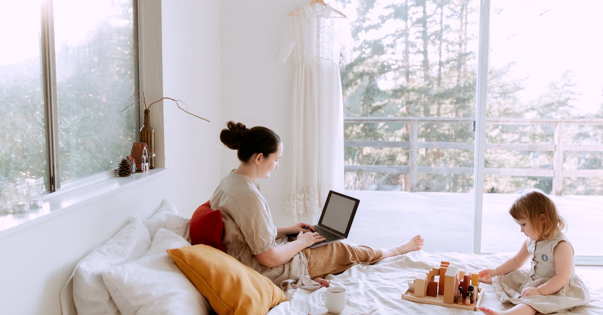 Is it possible to play Splitscreen Online? [duplicate] - Side view of cute toddler girl sitting on bed barefoot and playing with colorful wooden blocks while mother using laptop in bed enjoying morning coffee
