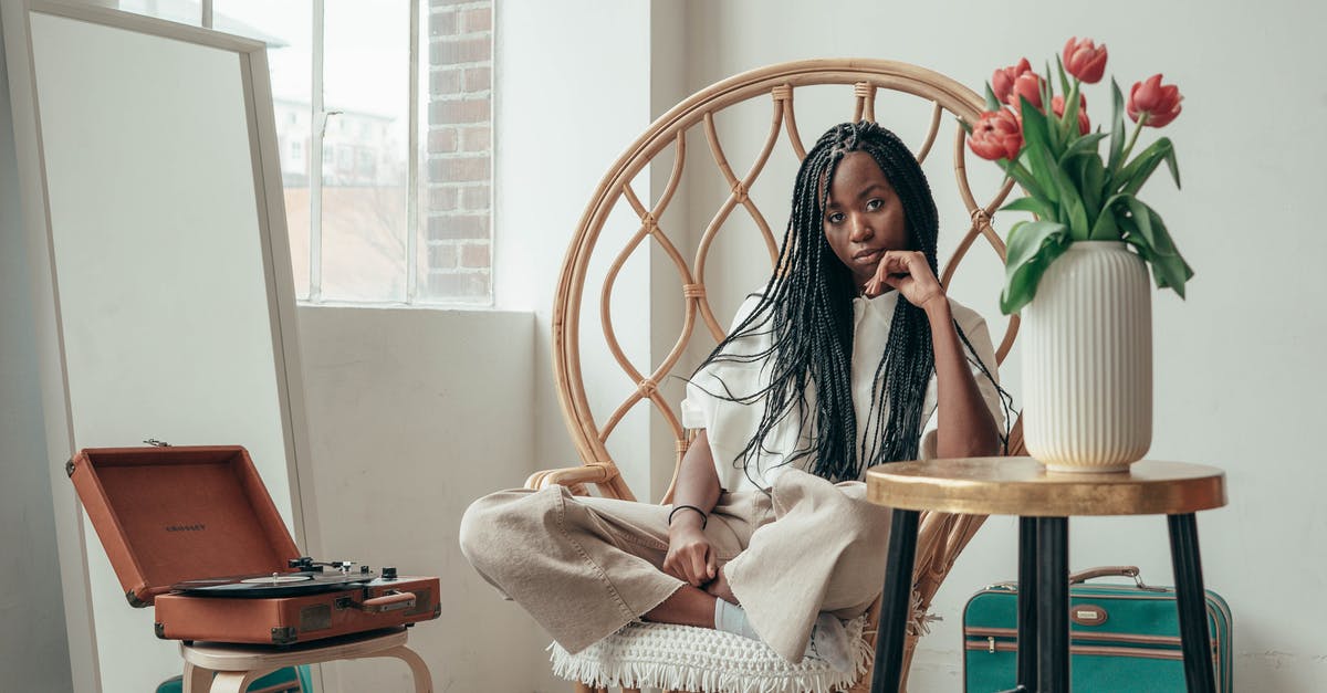 Is it possible to record clips less than a minute in length? - Serious young African American female millennial sitting on bamboo chair with crossed legs near table with vase of fresh tulips and listening to music via vinyl record
