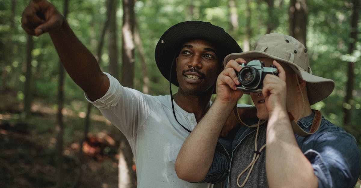 Is it possible to travel into / interact with NPCs in enemy faction territories? - Young black male traveler indicating with finger near anonymous best friend taking photo on camera in woods