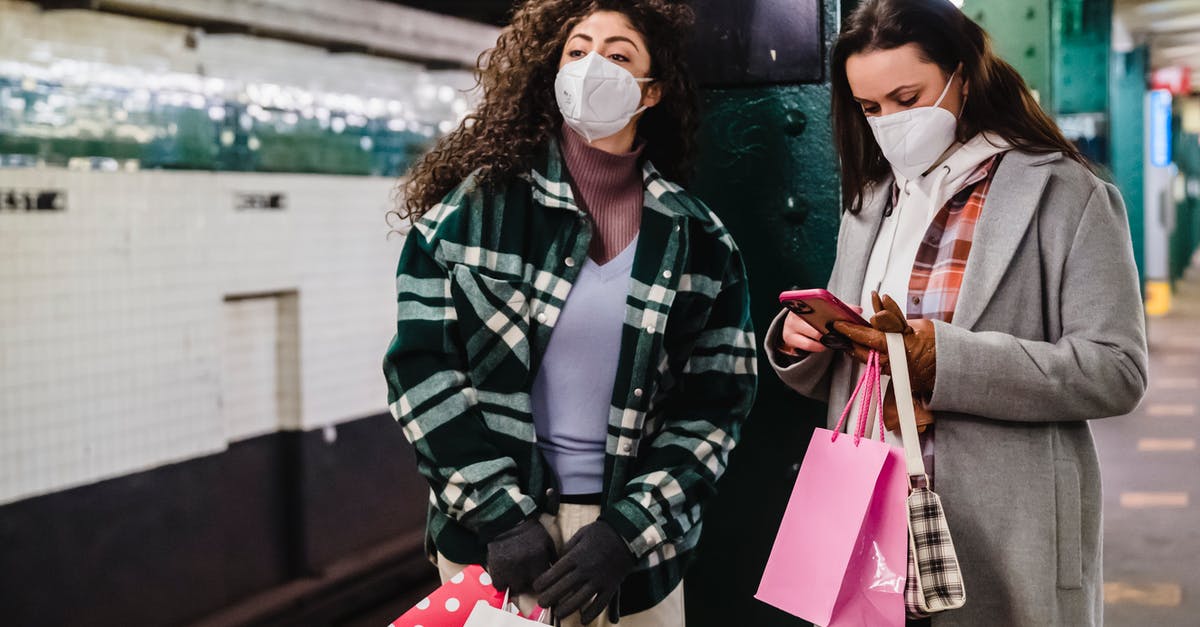 Is it safe to use EMP devices near agent Sharp? - Female in protective mask using mobile phone while waiting for train on platform of subway station with friend standing with gift bags