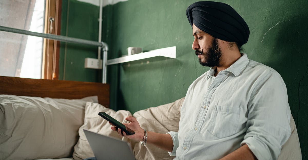 Is Quiet connected? - Bearded Indian businessman in casual clothes with serious expression on face texting on mobile and surfing net on laptop while working in comfort of quiet room Is Quiet connected? - Bearded Indian businessman in casual clothes with serious expression on face texting on mobile and surfing net on laptop while working in comfort of quiet room