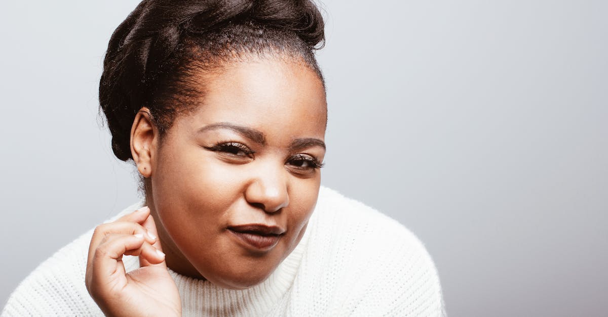 Is Sly Trilogy compatible with Cross-Buy? - Positive plus size African American female wearing cozy white knitted sweater standing on gray background in studio and looking at camera with half closed eyes