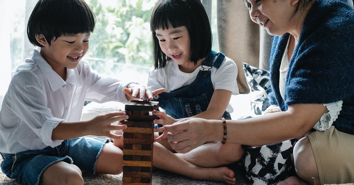 Is the tower game shown in the 'Hero Wars' ad a real game? - Full body of happy ethnic little children with elderly grandmother sitting on floor and constructing wooden tower while playing board game at home