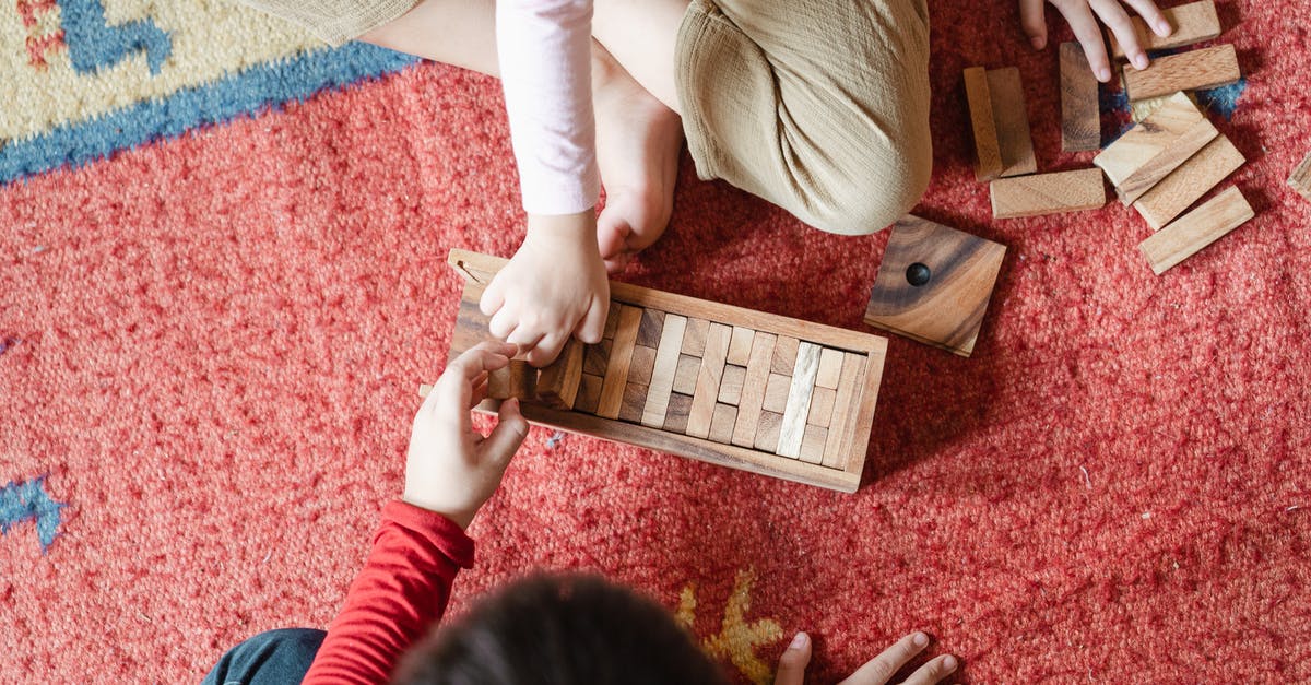 Is the tower game shown in the 'Hero Wars' ad a real game? - Top view of anonymous barefoot boy and girl in casual clothes sitting on floor carpet and playing with wooden blocks of jenga tower game