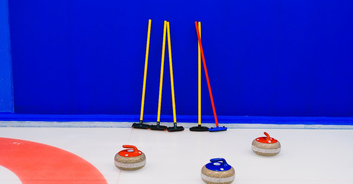 Is there a correlation between my collection and the arena cards? - Granite curling stones with colorful handles placed on ice sheet near set of shrubs at blue wall in arena during game