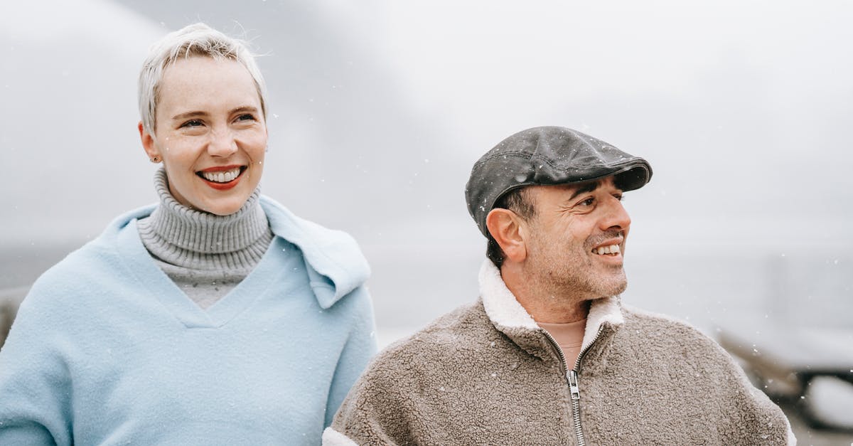 Is there a <10 relationship cap with bachelor/bachelorettes who aren't your spouse? - Cheerful woman with male partner in cap enjoying misty town while spending weekend together and looking away