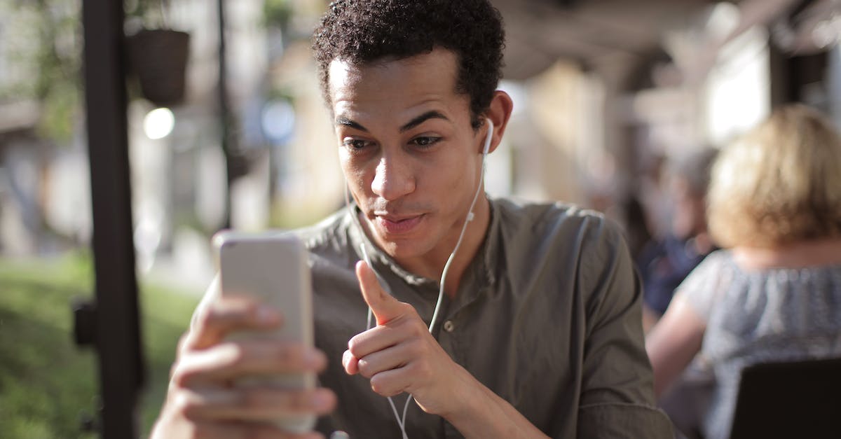 Is there a point to interacting with Pokemon in your lobby/city area? - Smiling African American male in casual clothing sitting in street cafe and talking via video chat while chilling in city and using mobile phone
