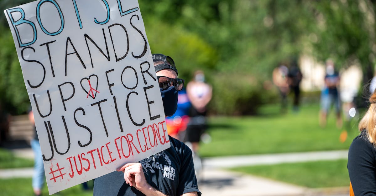 Is there a point to interacting with Pokemon in your lobby/city area? - Anonymous male activist wearing protective mask and sunglasses demonstrating placard with antiracist slogan during protest meeting in city park