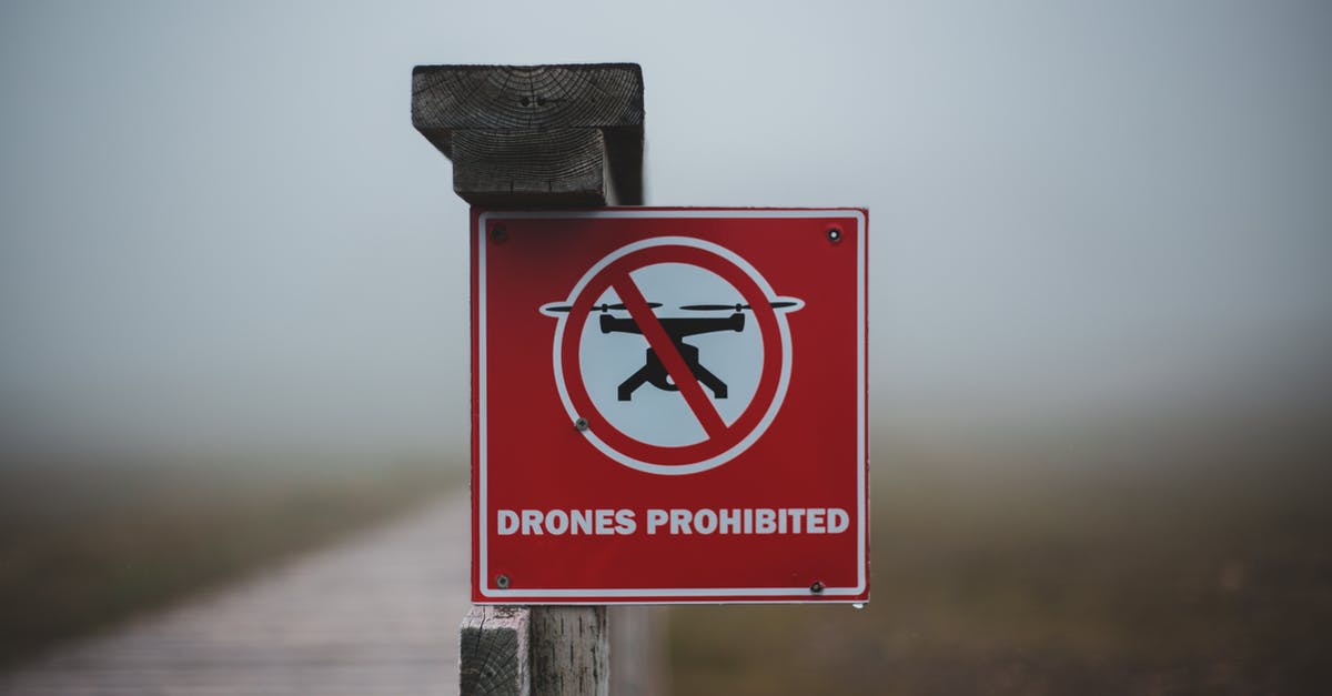 Is there a quiet way to take out a drone without causing the enemies to start searching? - Sign prohibiting use of drones placed on wooden fence near wooden walkway in field in foggy day