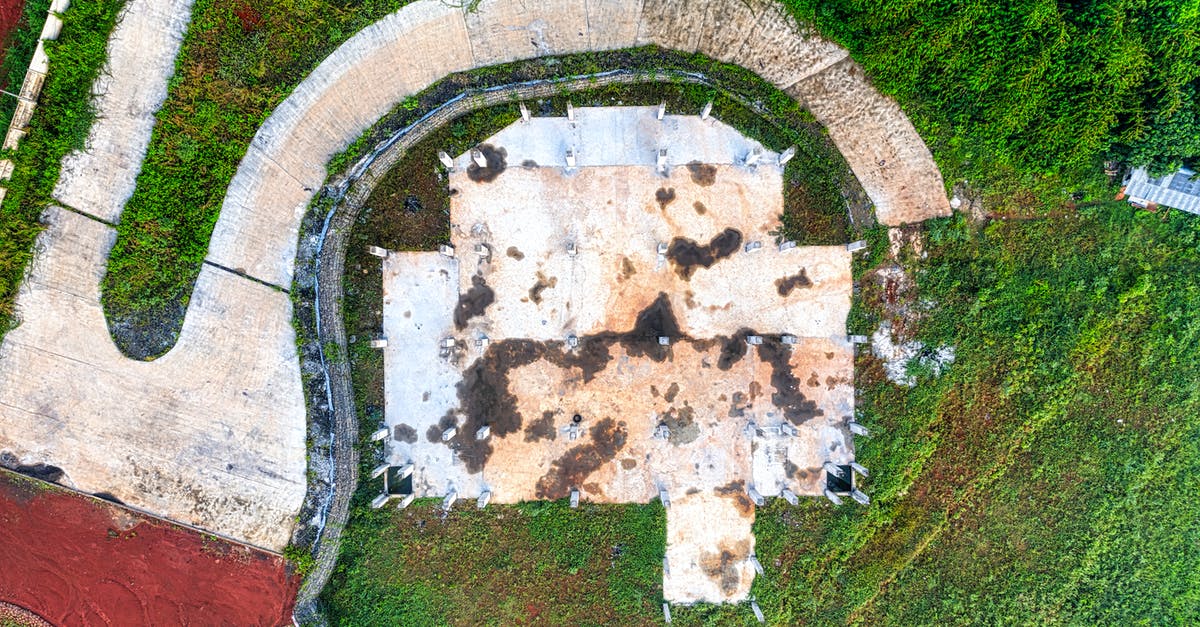 Is there a quiet way to take out a drone without causing the enemies to start searching? - Drone view of aged asphalt curvy road near old abandoned warehouse with damaged roof in verdant field Is there a quiet way to take out a drone without causing the enemies to start searching? - Drone view of aged asphalt curvy road near old abandoned warehouse with damaged roof in verdant field