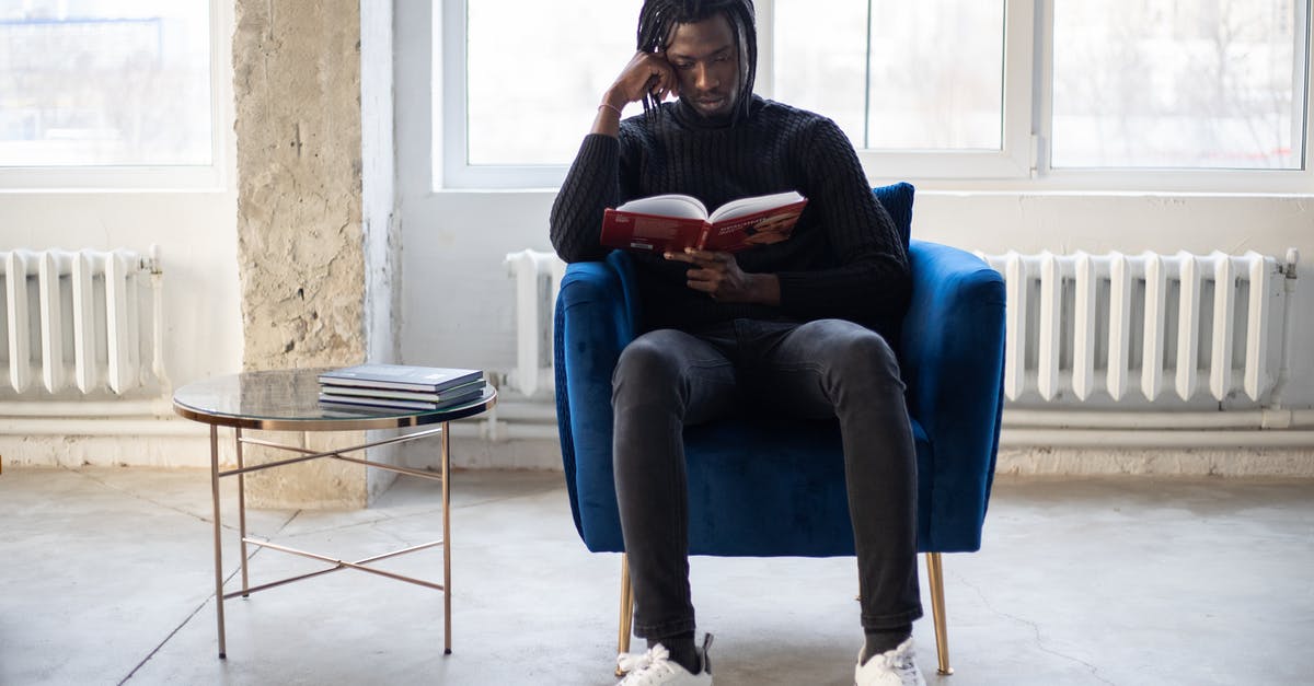 Is there a story behind the Doom Guy dolls? - Full body of young African American male reading book in comfortable armchair near table with literature in hall in daytime