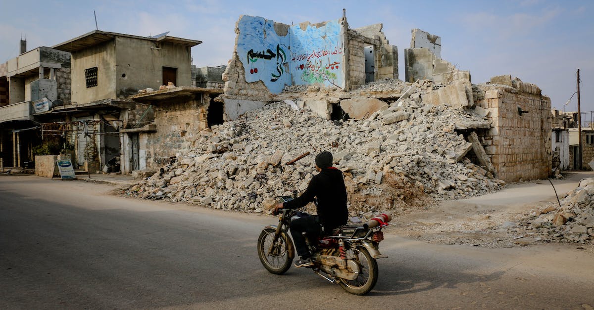 Is there a way to destroy spike balls? [duplicate] - Full body side view of anonymous man riding motorcycle on road near heap of ruins and destroyed buildings in poor district