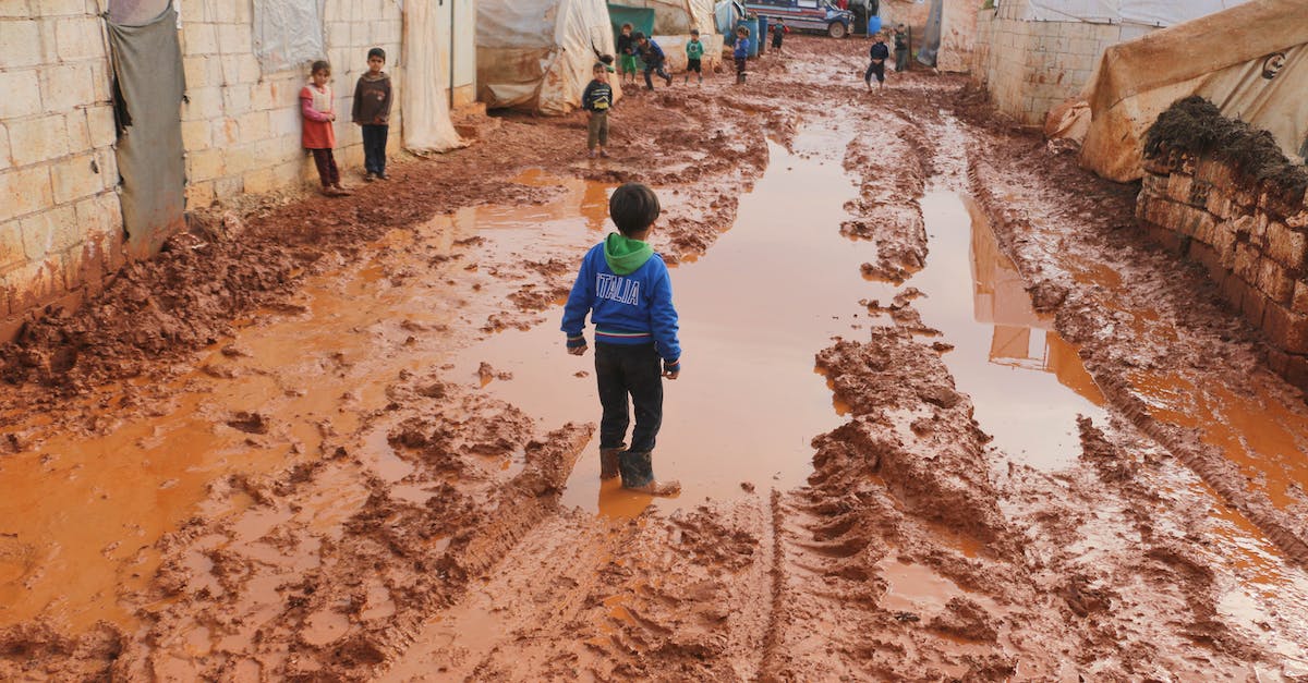 Is there a way to get rid of dirt patches? - Group of children standing on dirty wet ground with puddles between old tents in refugee camp with in poor settlement