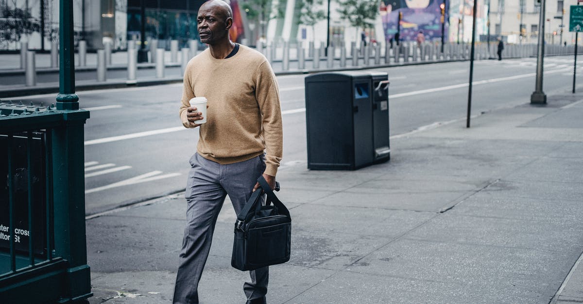 Is there a way to go quickly to Mergo's loft? - Full body of pensive African American male walking on pavement near asphalt road with takeaway coffee and black handbag in hand Is there a way to go quickly to Mergo's loft? - Full body of pensive African American male walking on pavement near asphalt road with takeaway coffee and black handbag in hand