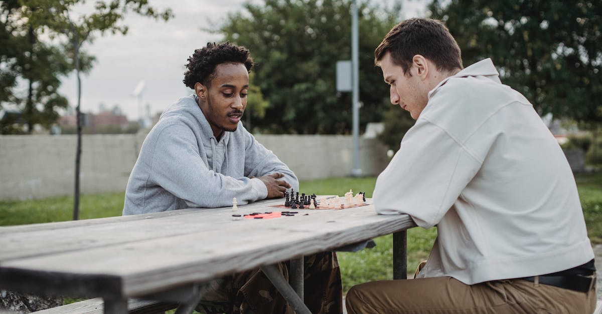 Is there a way to play the Battle Maison with friends over online? - Side view of serious young guy playing chess with African American friends while spending time in city park