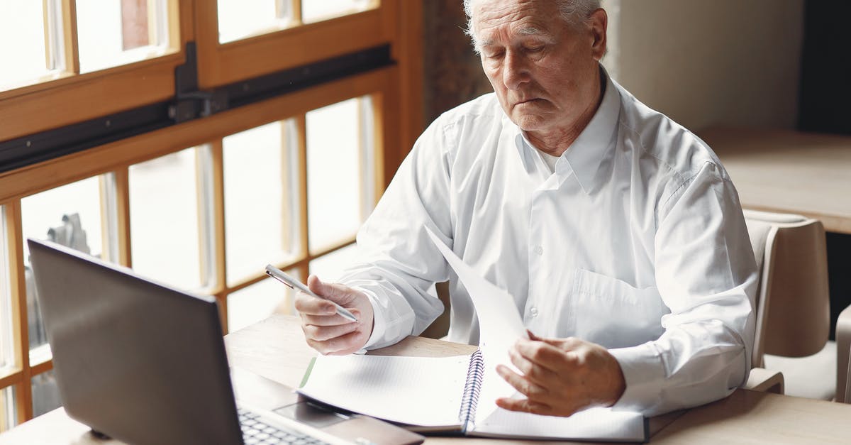 Is there a way to use an IOS Clash of Clans Account on my Computer? - Serious gray haired aged man in white shirt sitting at table and browsing laptop while checking notes in modern office
