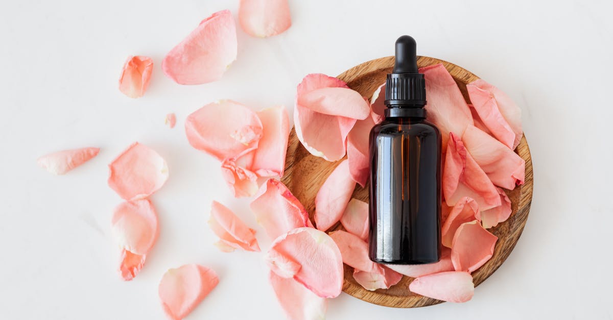 Is there an overhead view? - Top view of empty brown bottle for skin care product placed on wooden plate with fresh pink rose petals on white background isolated